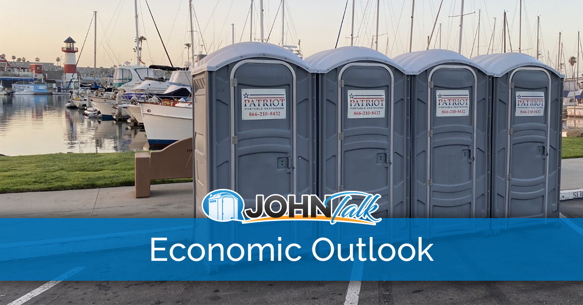 Gray portable toilets next to water with boats and a lighthouse in the background
