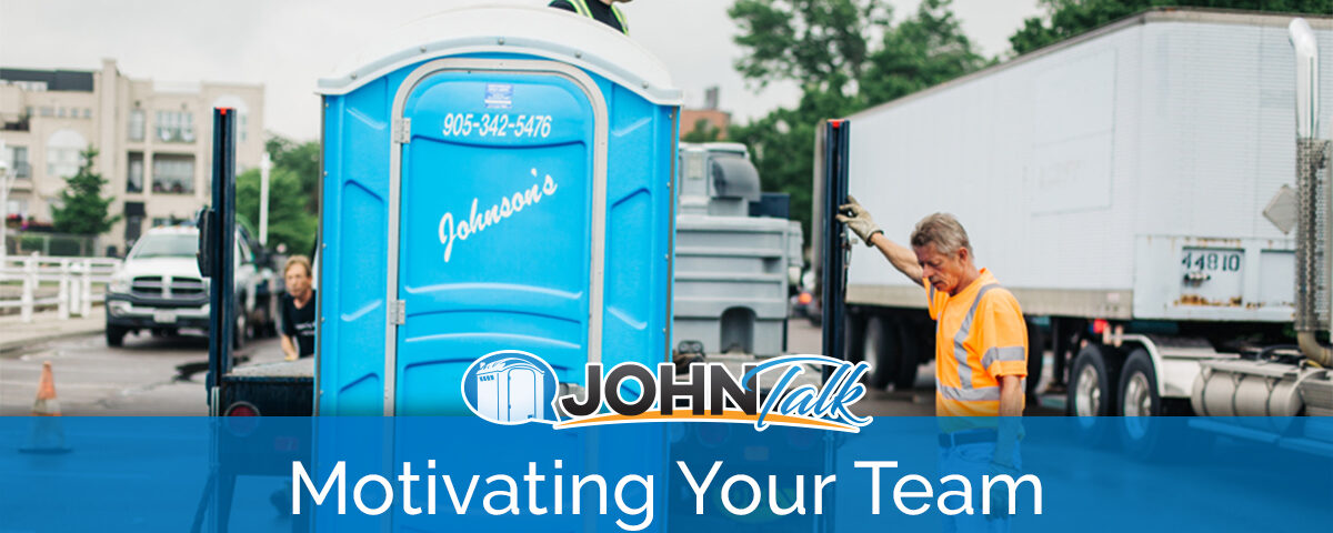 Two workers unloading a blue portable toilet from the back of a truck