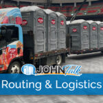 A colorful truck pulling a trailer loaded with several gray portable toilets inside a stadium