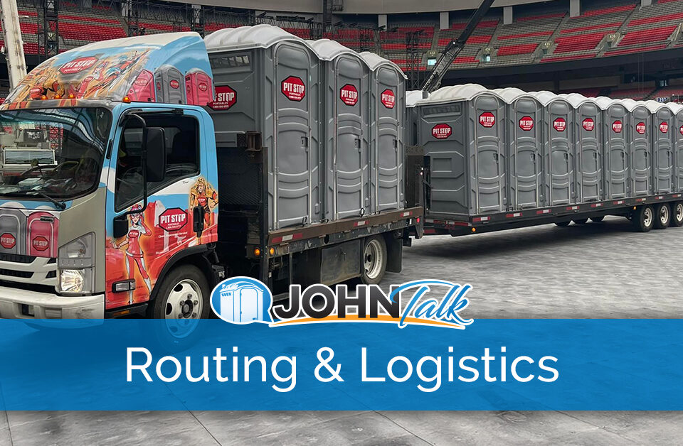 A colorful truck pulling a trailer loaded with several gray portable toilets inside a stadium
