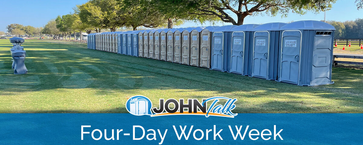 A long row of gray and tan portable toilets in a grassy area, with some portable sinks nearby