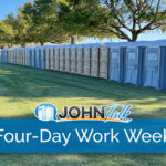 A long row of gray and tan portable toilets in a grassy area, with some portable sinks nearby