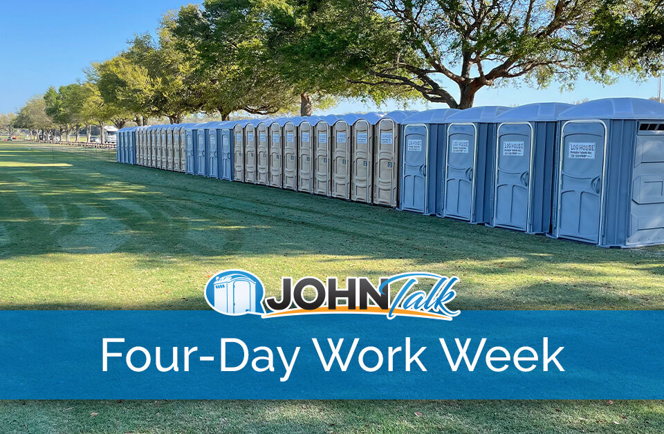 A long row of gray and tan portable toilets in a grassy area, with some portable sinks nearby
