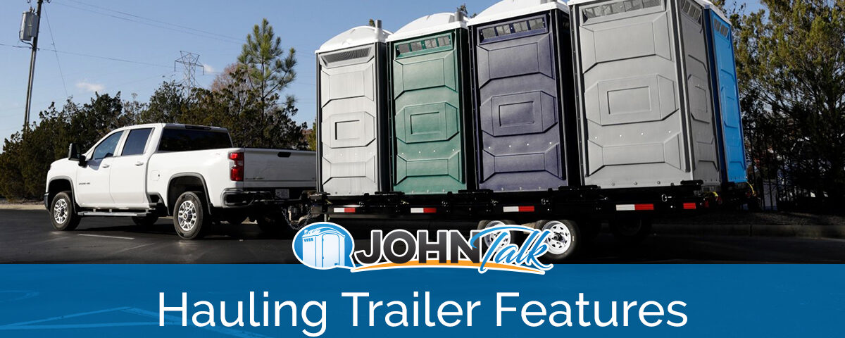 A white pickup pulling a hauling trailer with several portable toilets of various colors