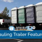 A white pickup pulling a hauling trailer with several portable toilets of various colors