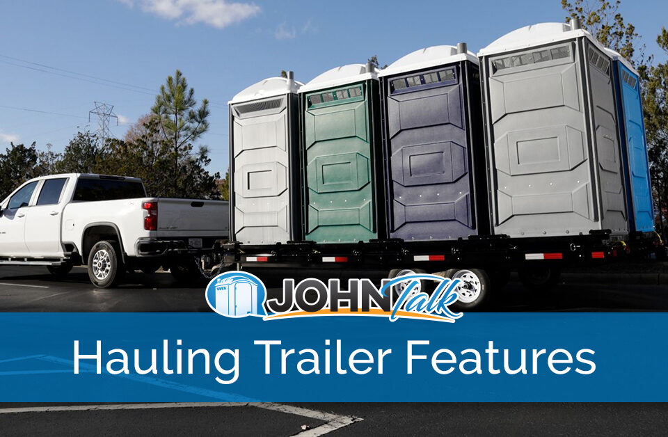 A white pickup pulling a hauling trailer with several portable toilets of various colors