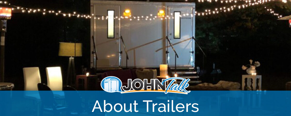 An outdoor patio at night with string lights hanging and a portable restroom trailer in the background