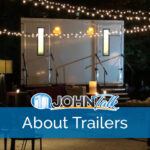 An outdoor patio at night with string lights hanging and a portable restroom trailer in the background