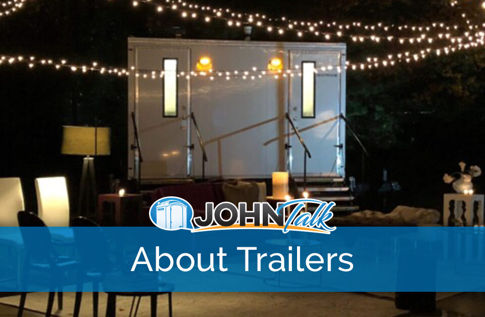 An outdoor patio at night with string lights hanging and a portable restroom trailer in the background