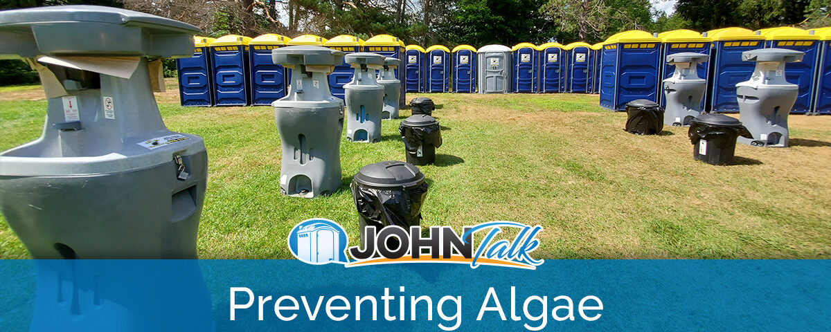 A group of portable sinks and trash cans in a grassy field with a row of blue and yellow portable toilets in the background