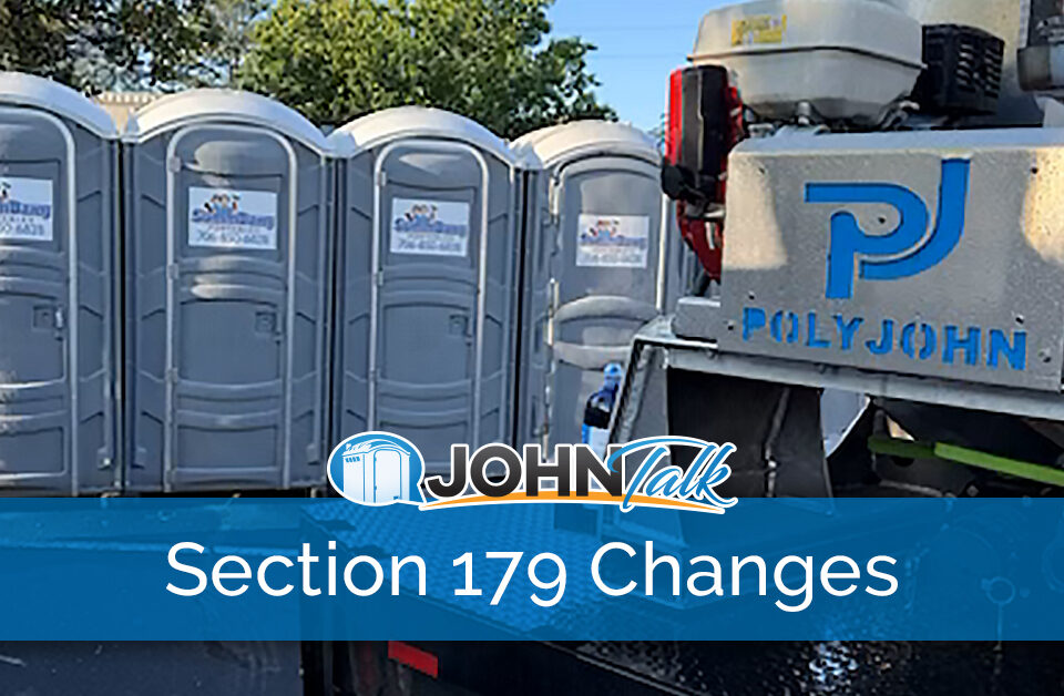 A closeup of a slide-in vacuum unit on a truck with a row of gray portable toilets in the background