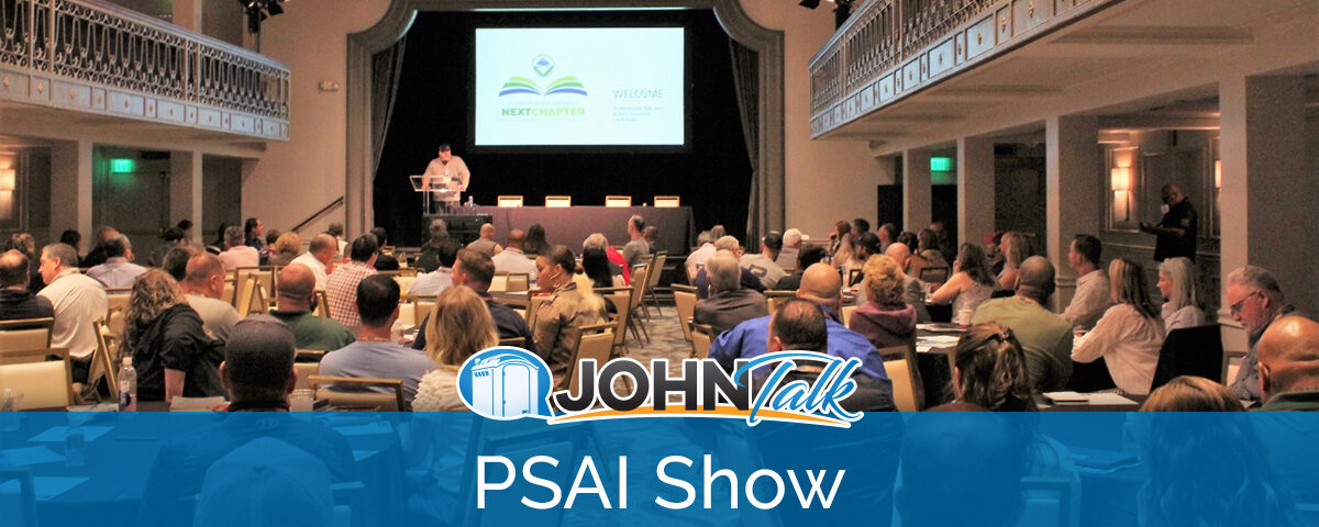 A group of people sitting at tables watching a presentation by a speaker on a stage