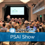A group of people sitting at tables watching a presentation by a speaker on a stage