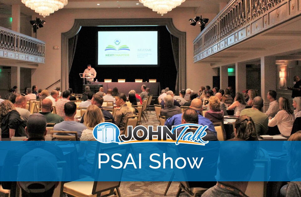 A group of people sitting at tables watching a presentation by a speaker on a stage