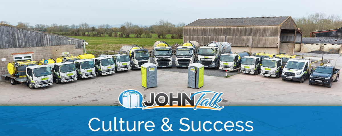A lineup of portable toilet service trucks in a parking lot with two gray and lime portable toilets in front of them