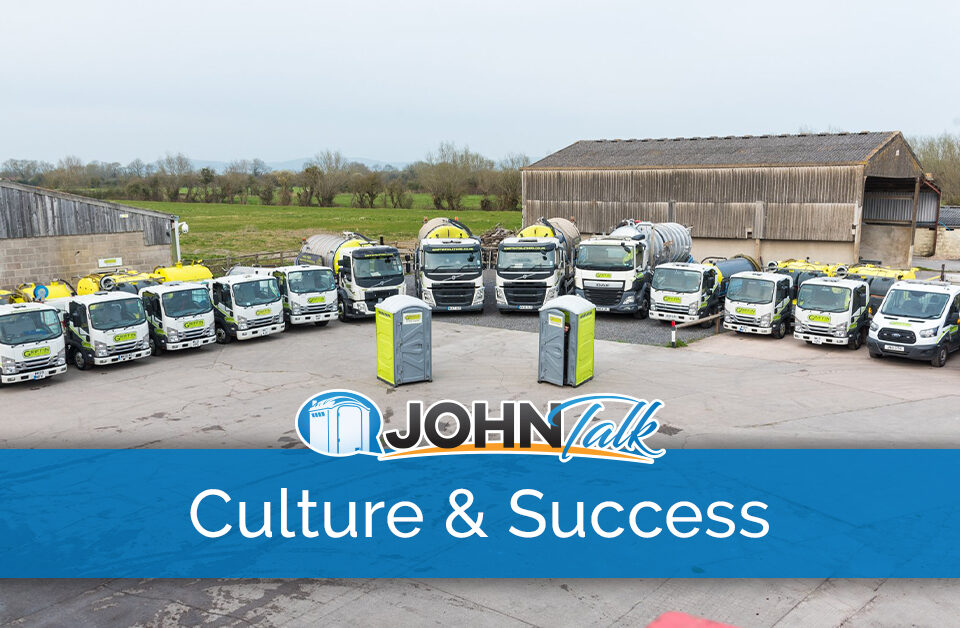 A lineup of portable toilet service trucks in a parking lot with two gray and lime portable toilets in front of them