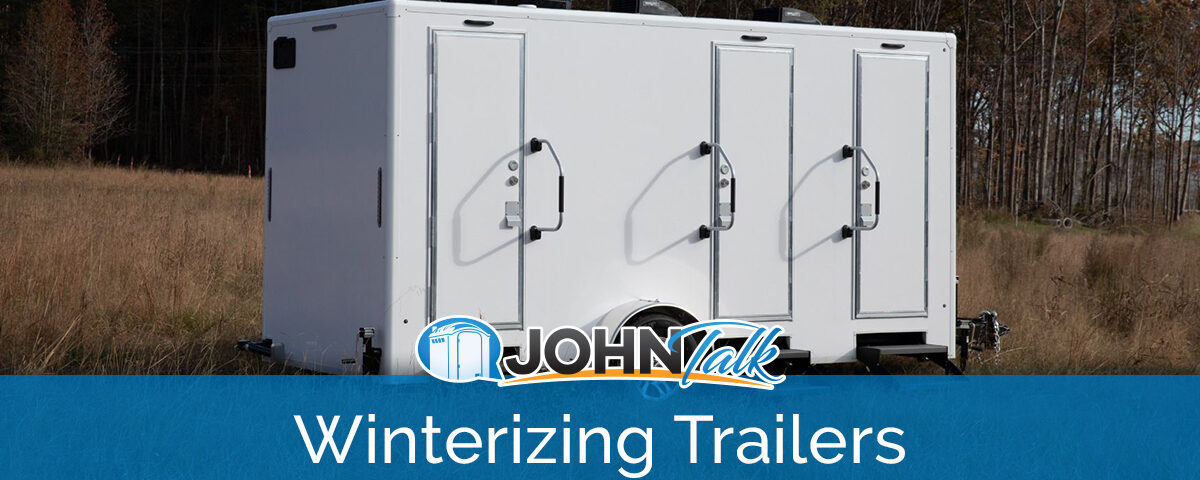 A white luxury restroom trailer in a grassy field with trees in the background