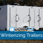 A white luxury restroom trailer in a grassy field with trees in the background