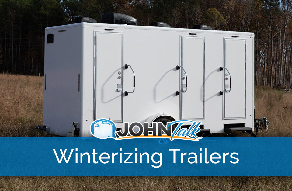 A white luxury restroom trailer in a grassy field with trees in the background