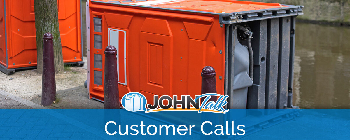 An orange portable toilet tipped over on the sidewalk next to a canal