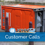 An orange portable toilet tipped over on the sidewalk next to a canal