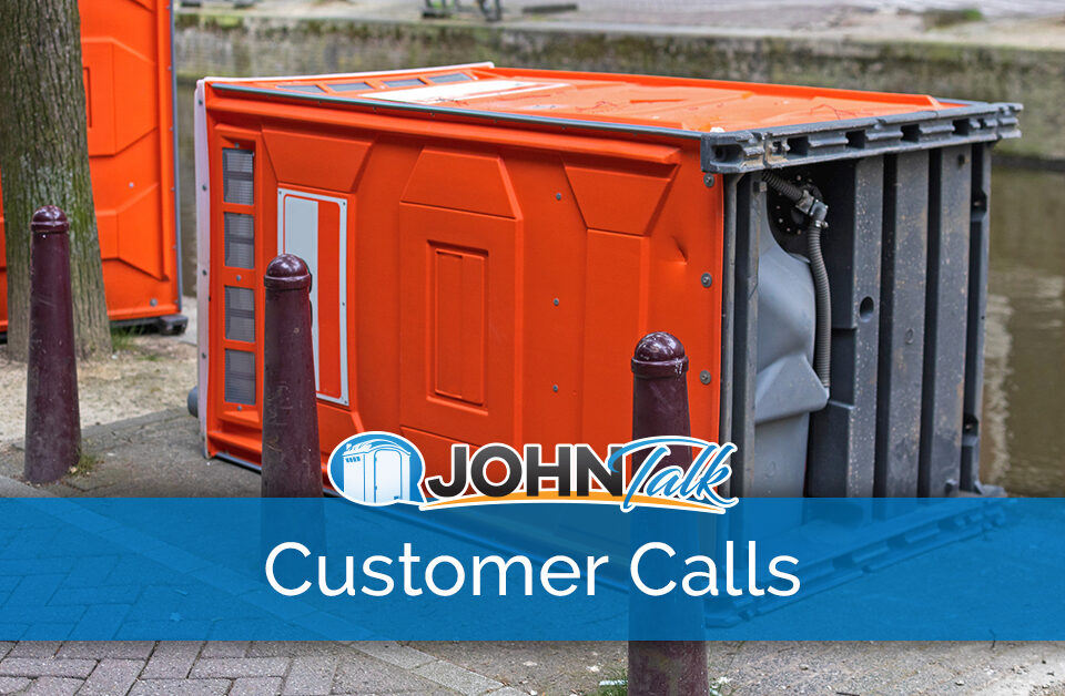 An orange portable toilet tipped over on the sidewalk next to a canal