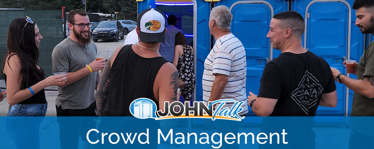 A crowd of people standing by a row of blue portable toilets
