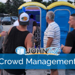 A crowd of people standing by a row of blue portable toilets