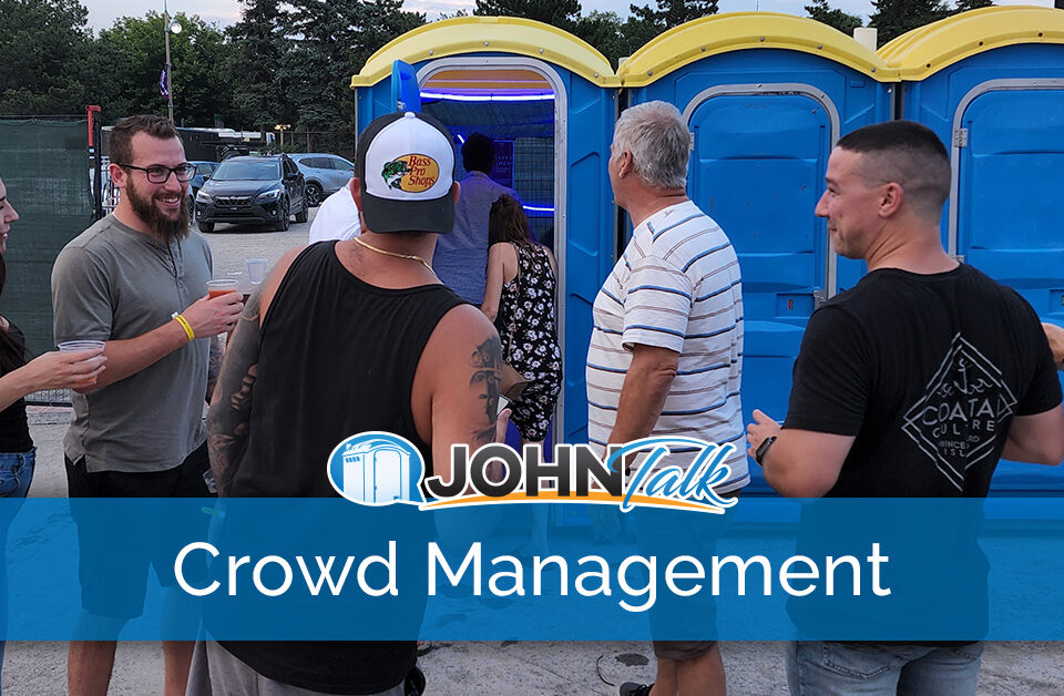 A crowd of people standing by a row of blue portable toilets