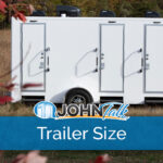 A white portable restroom trailer sitting in a grassy area