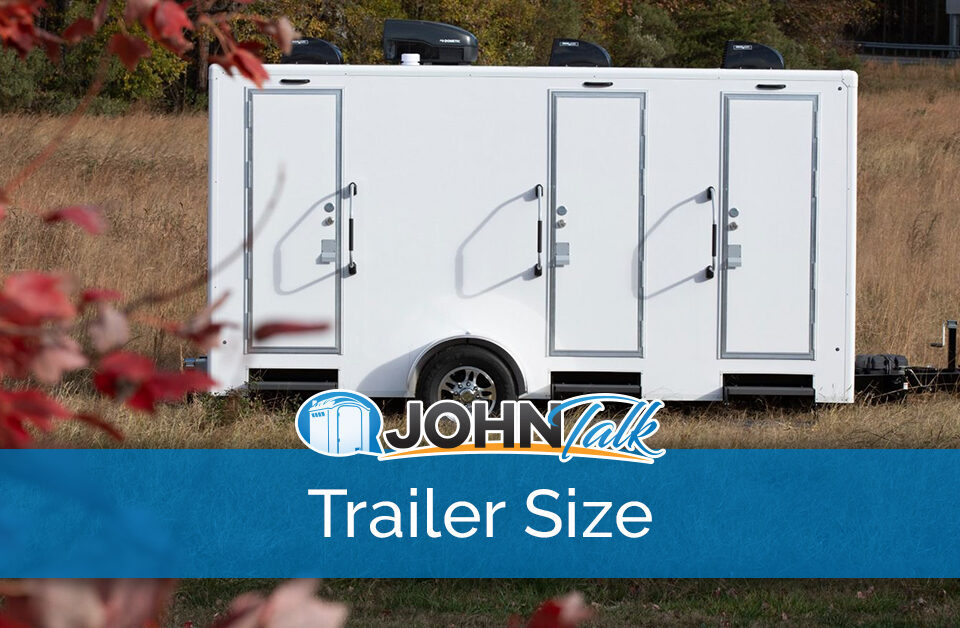 A white portable restroom trailer sitting in a grassy area